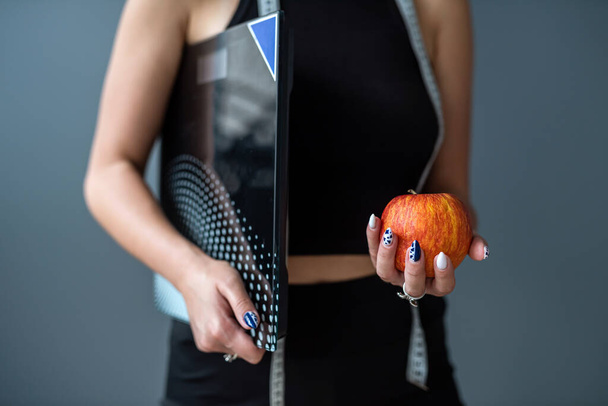 Fiatal boldog sport sport fitness edző oktató nő visel fekete sport ruha tartja alma mérőszalag súlya elszigetelt szürke háttér. Sport edzés koncepció - Fotó, kép