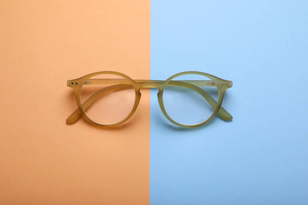 Glasses with corrective lenses on color background, top view - Фото, изображение