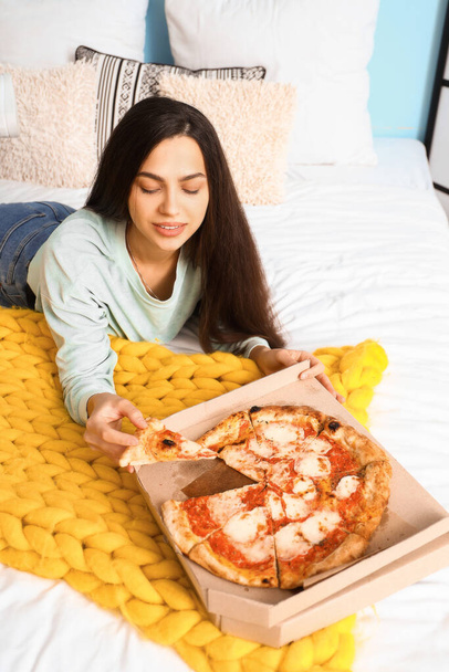 Young woman with tasty pizza lying in bedroom - Foto, Bild