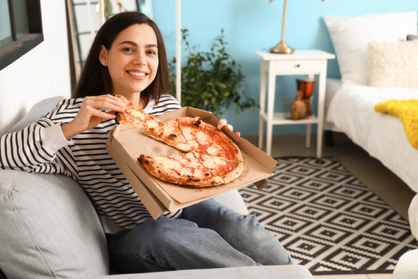 Молода жінка зі смачною піцою сидить на дивані вдома
 - Фото, зображення