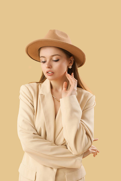 Модна молода жінка в стильній куртці і капелюсі на бежевому фоні
 - Фото, зображення
