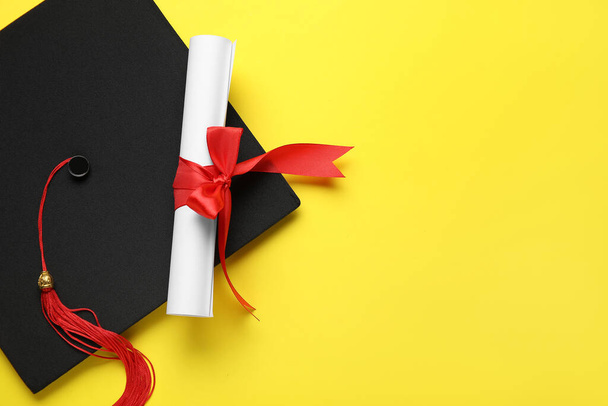 Diploma with red ribbon and graduation hat on yellow background - 写真・画像