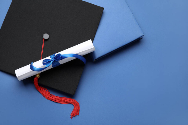 Diplôme avec ruban et chapeau de graduation sur fond bleu - Photo, image