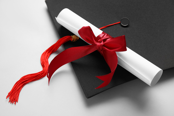 Diploma with red ribbon and graduation hat on white background - Foto, imagen