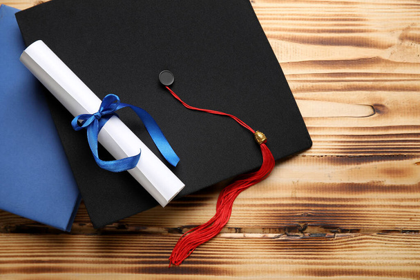 Diplôme avec ruban bleu, chapeau de graduation et livre sur table en bois - Photo, image