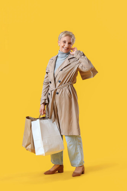 Beautiful mature woman with shopping bags on yellow background - Photo, image