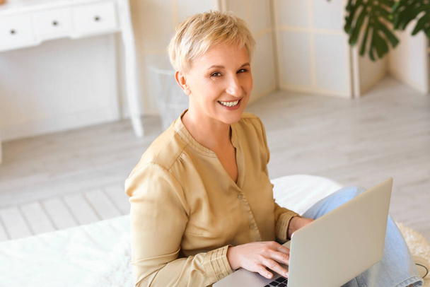 Femme mûre utilisant un ordinateur portable dans la chambre - Photo, image
