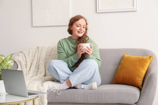 Красива руда жінка з чашкою чаю, що сидить на дивані вдома
 - Фото, зображення