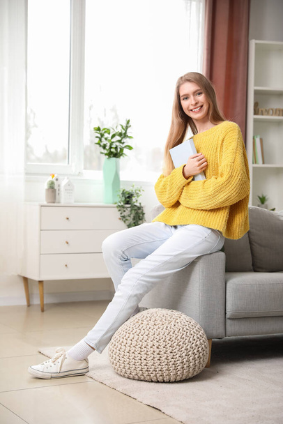 Молодая женщина с книгой сидит дома на диване - Фото, изображение