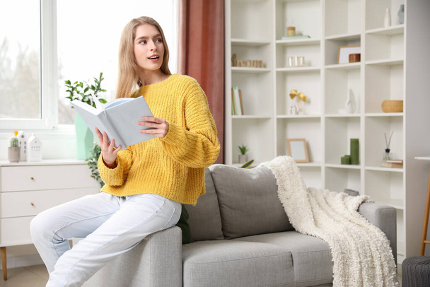 Young woman reading book on sofa at home - Photo, image