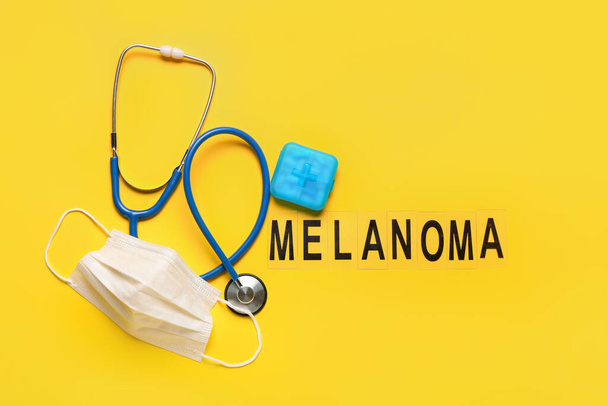 単語メラノーマ,黄色の背景に錠剤、医療用マスクと聴診器付き容器 - 写真・画像