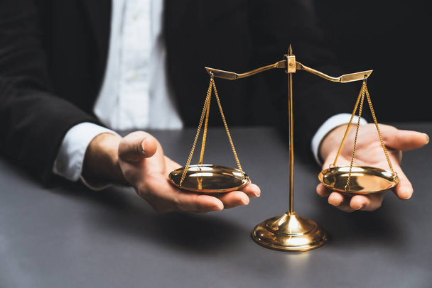 Advocaat in een zwart pak zit aandachtig op zijn bureau met een gouden weegschaal evenwicht, symbool van juridische rechtvaardigheid en integriteit, evenwichtige en ethische besluitvorming in de rechtbank. gelijkheid - Foto, afbeelding