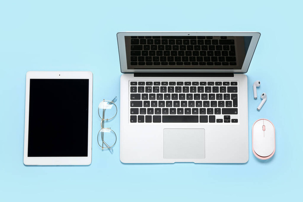Samenstelling met laptop, bril en oortjes op blauwe achtergrond - Foto, afbeelding