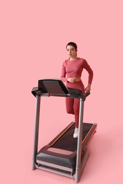 Sporty young woman training on treadmill against pink background - Фото, зображення