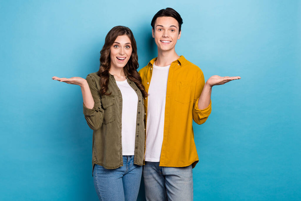 Photo of stylish wearing clothes boyfriends with girlfriend hold arms empty space proposition choose best offer isolated on blue color background. - Fotoğraf, Görsel