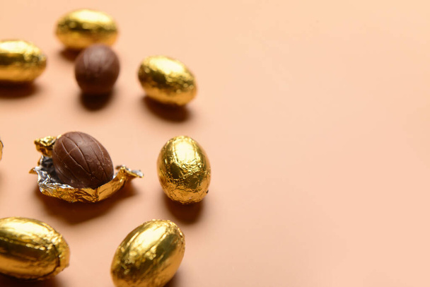 Bej arka planda altın folyoyla çikolatalı Paskalya yumurtaları. - Fotoğraf, Görsel