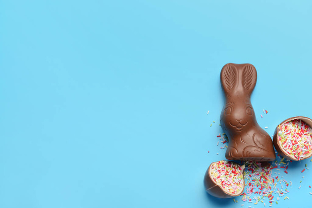 Kırık çikolatalı Paskalya yumurtası, mavi arka planda serpiştirilmiş tavşancık. - Fotoğraf, Görsel