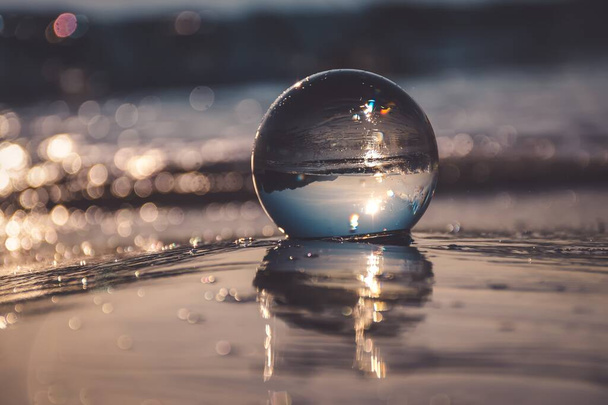 Abstraktní nápad s vodou se zajímavým efektem. Skleněná koule na rozmazaném pozadí na přímořské pláži v polské Gdyni. Fotografie s mělkou hloubkou pole. - Fotografie, Obrázek