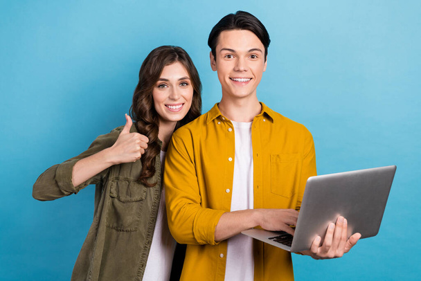 Foto de bonito alegre casal vestir camisas mostrando polegar para cima mensagens de texto moderno dispositivo isolado azul cor de fundo. - Foto, Imagem