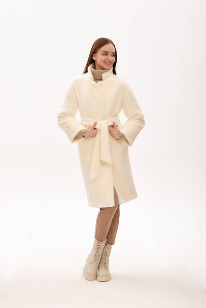 Μοντέρνο κορίτσι με αυτοπεποίθηση σε ένα ελαφρύ γούνινο παλτό. Σύγχρονη τάση της μόδας για γούνες από faux γούνα. Υπόδειγμα ποζαρίσματος σε γούνα σε ανοιχτό φόντο. - Φωτογραφία, εικόνα