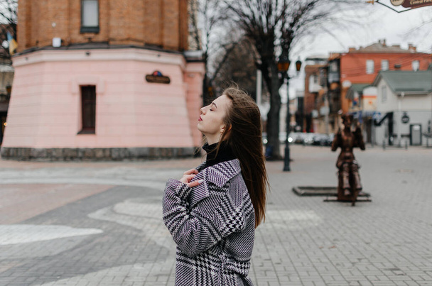 Pembe bir binanın önünde paltolu bir kadın duruyor. - Fotoğraf, Görsel