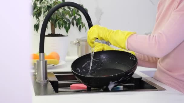 Une femme en gants jaunes lave une casserole dans une cuisine blanche moderne. Propreté à la maison - Séquence, vidéo
