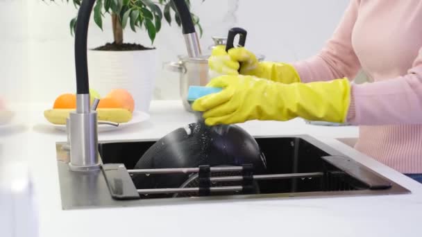 Limpieza en la cocina. Una mujer con guantes amarillos lava una sartén en una cocina blanca moderna. Concepto de limpieza - Metraje, vídeo