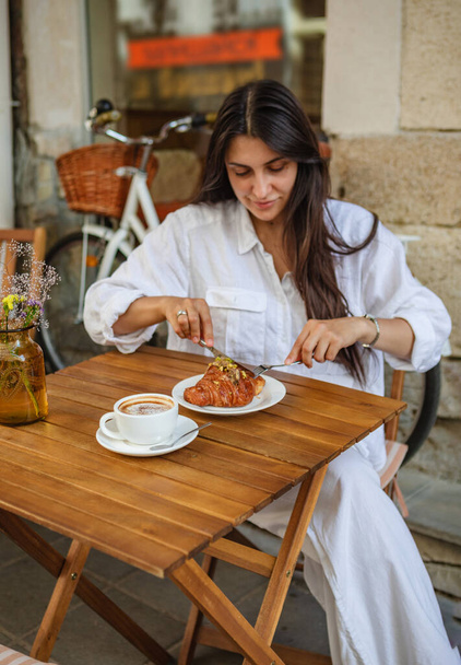 Na letní terase si žena vychutnává snídani s křupavými croissanty a kávou - Fotografie, Obrázek