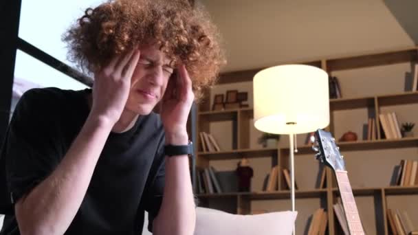 A young man with a strange hairstyle is suffering from a headache. A curly red-haired boy and a migraine. Headache. Misfortune. - Footage, Video