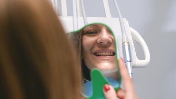 Frau bewundert Lächeln in Zahnarztpraxis. Glückliche junge Frau lächelt, während sie ihre perfekte Zahngesundheit im Spiegel in Großaufnahme überprüft. - Filmmaterial, Video