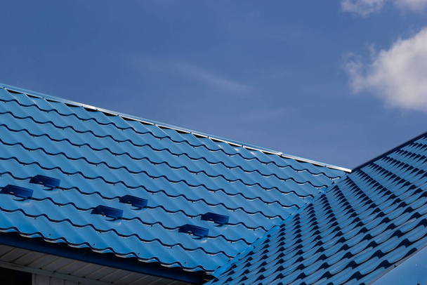 The roof of a house covered with sheets of blue metal tiles against the background of the sky on a summer day. Business selling building materials or repairing house roofs. - Photo, Image
