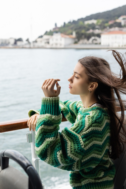 Vue latérale de la jeune femme en pull debout près de la rampe sur le yacht en Turquie  - Photo, image