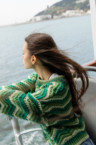 Seitenansicht einer jungen brünetten Frau im Strickpullover mit Blick auf das Meer während einer Kreuzfahrt auf einer Jacht in der Türkei  - Foto, Bild