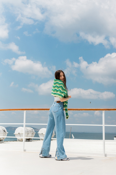 Усміхнена жінка в джинсах і светр дивиться на камеру, стоячи на яхті в Туреччині.  - Фото, зображення