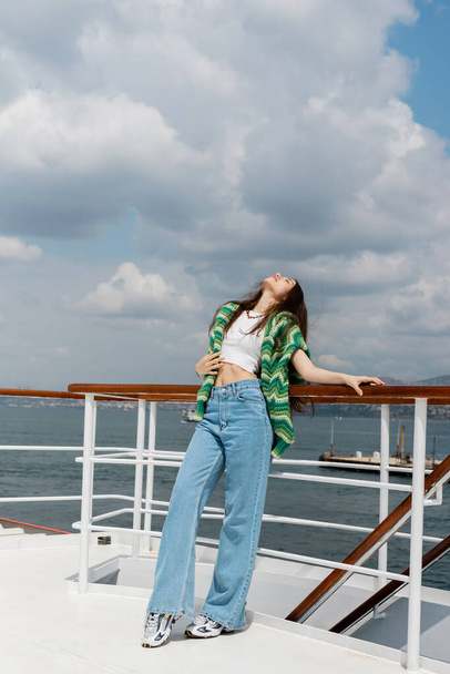 Młoda kobieta w swetrze i dżinsach stojąca przy poręczy jachtu w Turcji  - Zdjęcie, obraz