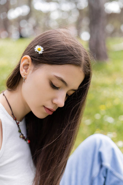 Brunette woman with daisy in hair spending time in park  - Foto, Bild