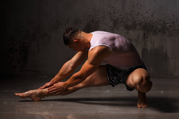 Bodybuilder επιδεικνύει τους μυς του και την εικόνα στο στούντιο στη βροχή. - Φωτογραφία, εικόνα