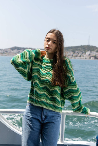 Portrait of brunette woman in knitted sweater looking at camera during cruise on ferry boat in Turkey  - Fotó, kép