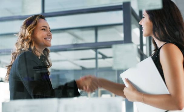 Its a pleasure to finally meet you. Low angle shot of two attractive young businesswomen shaking hands while standing in their office - Foto, imagen