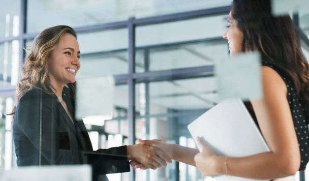 Nicely done. two attractive young businesswomen shaking hands while standing in their office - Foto, Imagen