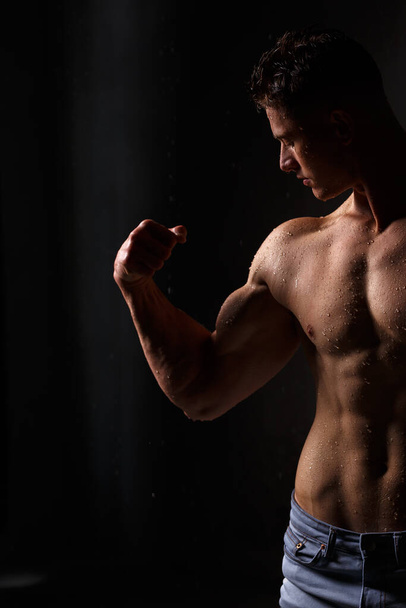 Bodybuilder affiche ses muscles et figure dans le studio sous la pluie. - Photo, image
