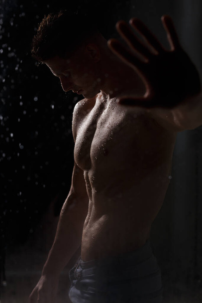 Culturista hace alarde de sus músculos y figura en el estudio bajo la lluvia. - Foto, Imagen