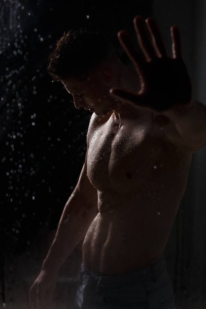 Culturista hace alarde de sus músculos y figura en el estudio bajo la lluvia. - Foto, Imagen