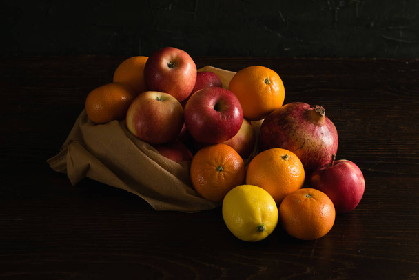 Fruit in a reusable bag. Earth day and zero waste concept. Apples, lemon, oranges and pomegranate on a dark wooden background - Foto, Bild