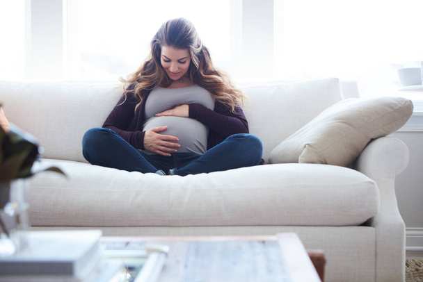 En malta odottaa tapaamistasi. Täyspitkä laukaus houkutteleva nuori raskaana oleva nainen istuu sohvalla kotona - Valokuva, kuva