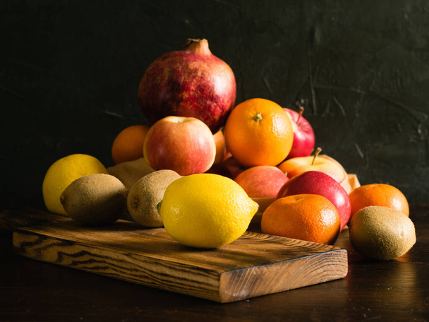 Obst in einem Mehrwegbeutel. Earth Day und Zero Waste Konzept. Orange, Zitrone, Apfel, Kiwi, Granatapfel und Holzschneidebrett auf dunklem Hintergrund. - Foto, Bild