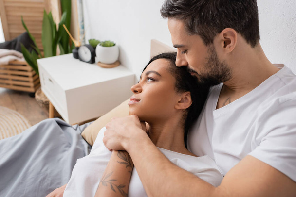 dreamy african american woman looking away near bearded boyfriend in bedroom at home - Photo, Image