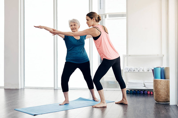 Θα ζήσεις πολύ καλύτερα μένοντας δραστήριος. ένας γυμναστής βοηθά μια ηλικιωμένη γυναίκα κατά τη διάρκεια ενός μαθήματος γιόγκα - Φωτογραφία, εικόνα