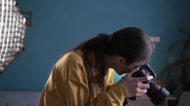 Γυναίκα φωτογράφος σε ένα εξοπλισμένο στούντιο φωτογραφίας ετοιμάζεται για το γύρισμα. Φωτάκι στούντιο με softbox. Έννοια της διαδικασίας εργασίας. Αντιγραφή χώρου - Πλάνα, βίντεο
