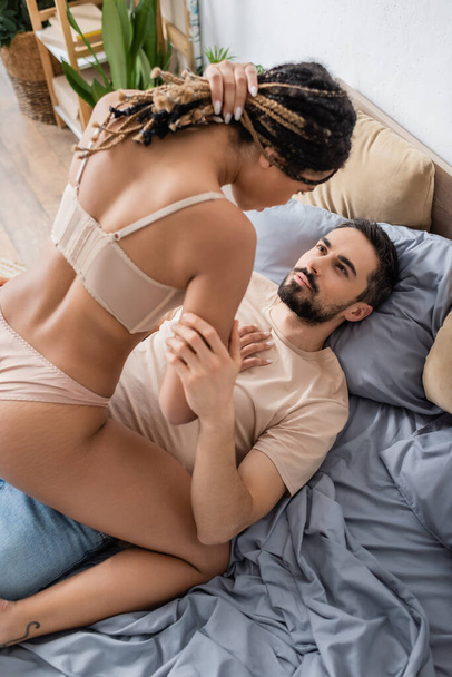 high angle view of passionate african american woman with dreadlocks seducing bearded man lying on bed at home - Φωτογραφία, εικόνα